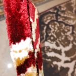 A close-up of the Autumn Horizon Rug showcasing intricate floral patterns in red, white, gold, and brown, with a folded corner revealing its underside. Handmade and available in Mumbai, India.