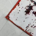 Discover the Jingle Frost Rug, a modern handmade rug with a plush texture and abstract patterns in white, red, and black, bordered by a red stitched edge.
