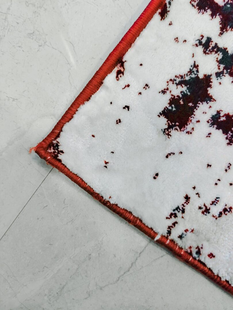 Discover the Jingle Frost Rug, a modern handmade rug with a plush texture and abstract patterns in white, red, and black, bordered by a red stitched edge.