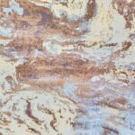 Close-up of the Milk Desert Rug featuring an abstract pattern in brown, purple, and blue tones, with a folded corner revealing its woven underside.