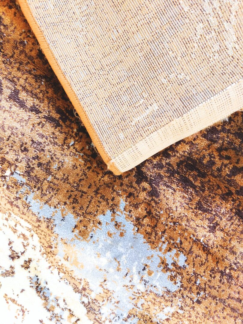 The Milk Desert Rug showcases a modern marbled design with swirling patterns in brown, beige, and light blue. A luxurious handmade rug for contemporary home decor