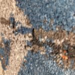 A collection of rolled-up rugs with the Nebula Script Rug in the foreground, showcasing a shaggy texture and vibrant colors like blue, gray, black, and orange.