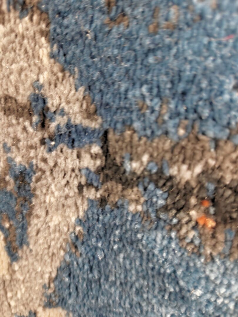 A collection of rolled-up rugs with the Nebula Script Rug in the foreground, showcasing a shaggy texture and vibrant colors like blue, gray, black, and orange.