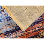 Two overlapping rugs, with the top rug showcasing a beige underside and the bottom rug featuring vibrant horizontal stripes in blue, orange, red, and yellow.